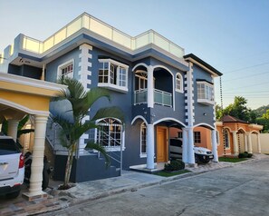 Une maison moderne à deux étages, dotée d’un balcon, de grandes fenêtres et d’une allée.