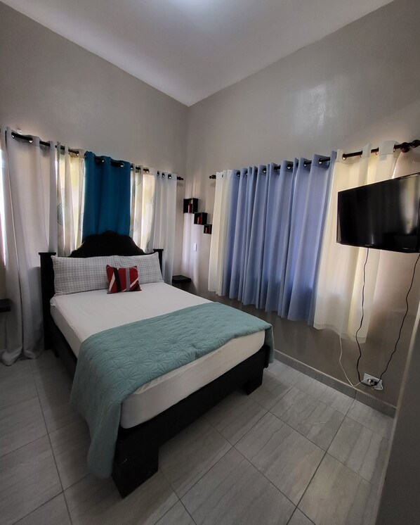 Une chambre à coucher avec un lit, des rideaux, un téléviseur et un téléviseur fixé au mur.