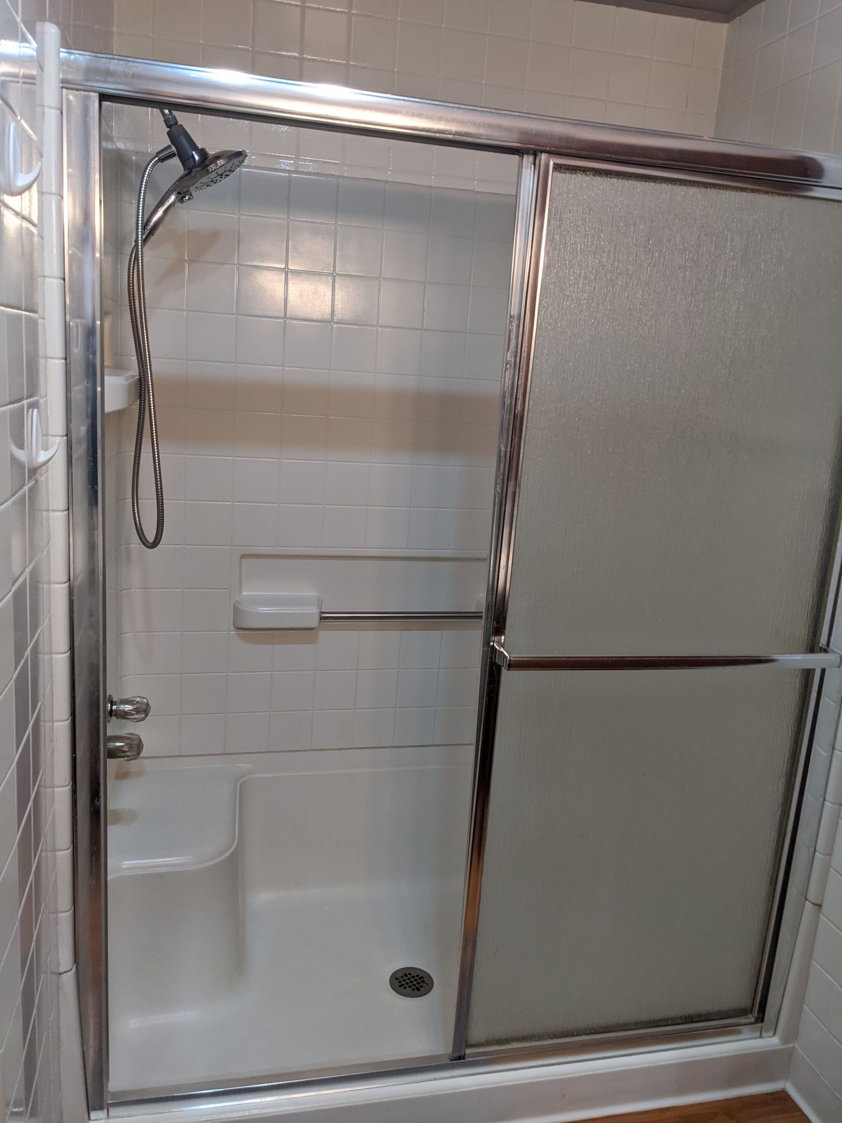 A glass-enclosed shower stall with a handheld showerhead, a control panel, and a drain.
