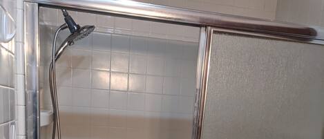 A glass-enclosed shower stall with a handheld showerhead, a control panel, and a drain.