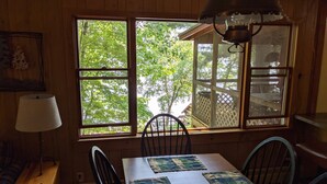 A dining area with a wooden table, four chairs, a lamp, and a window with a view of trees.