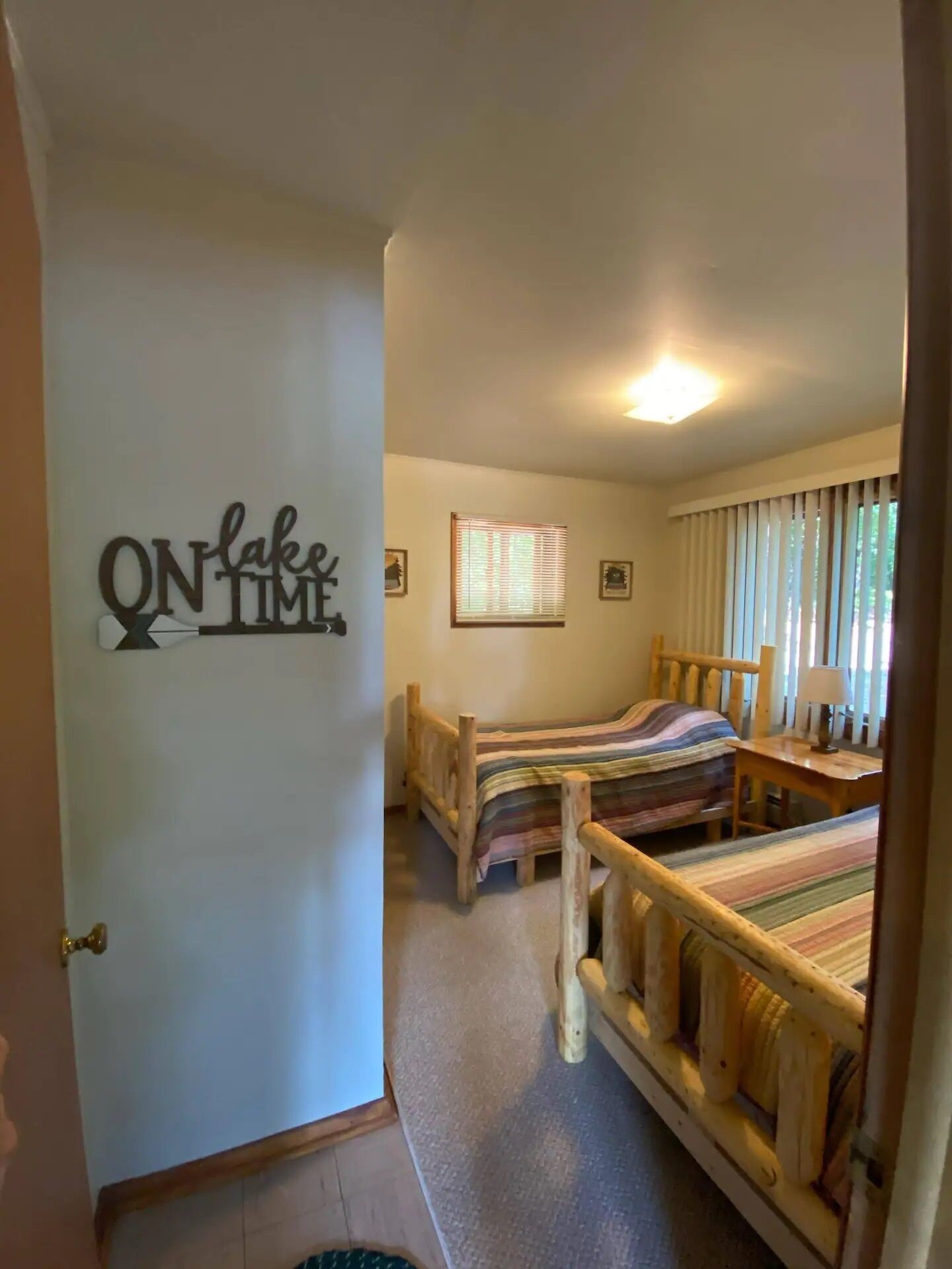 Une chambre avec deux lits en bois, un petit bureau et une fenêtre avec des stores.