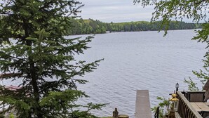 A lakeside deck with a wooden railing, a small dock, and a view of the lake.