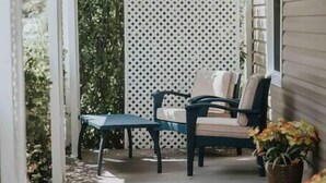 Eine überdachte Veranda mit Tisch und Stühlen, ein weißes Gitter und ein Blumentopf.