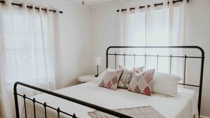 Ein ordentlich bezogenes Bett mit Metallgestell, weißer Bettwäsche und gemusterten Kissen.