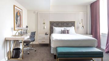 A hotel room with a bed, a desk, a chair, a bedside table, and a wall-mounted artwork.