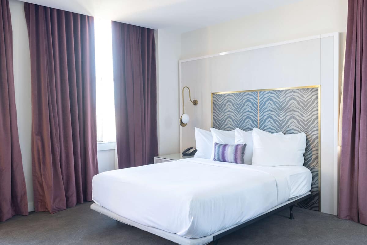 Een moderne hotelkamer met een groot bed, nachtkastje, lamp en een hoofdbord met patroon.