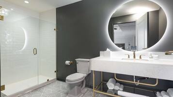 Un baño moderno con cabina de ducha de vidrio, inodoro, tocador con un espejo grande y suelo estampado.
