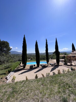 A pool area with four tall cypress trees, a clear blue sky, and a distant mountain range. - Cozy villa with a swimming pool, pétanque, and a barbecue (Saint-Saturnin-lès-Apt)