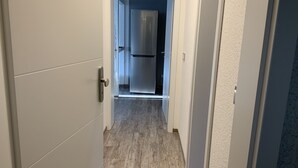 A narrow hallway with a wooden floor leading to a kitchen area with a stainless steel refrigerator. - Newly renovated apartment 65 m2 (Nordhausen)