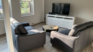 A modern living room with two grey sofas, a wooden coffee table, and a white entertainment unit with a flat-screen TV. - Newly renovated apartment 65 m2 (Nordhausen)