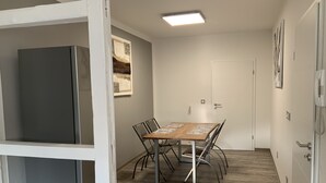 A small, well-lit room with a wooden table and chairs, a refrigerator, and a door with a light switch. - Newly renovated apartment 65 m2 (Nordhausen)