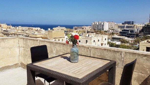 Un balcón con mesa y sillas, con vistas a un paisaje urbano que incluye edificios y el mar.
