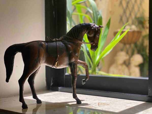 A bronze horse figurine on a reflective surface near a window with a view of greenery and a statue.