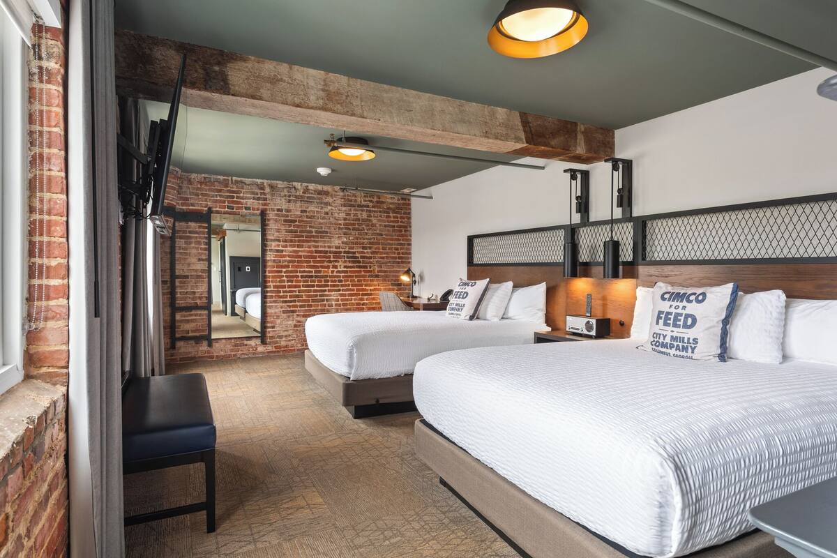A hotel room with two beds, a brick wall, and a modern ceiling design.