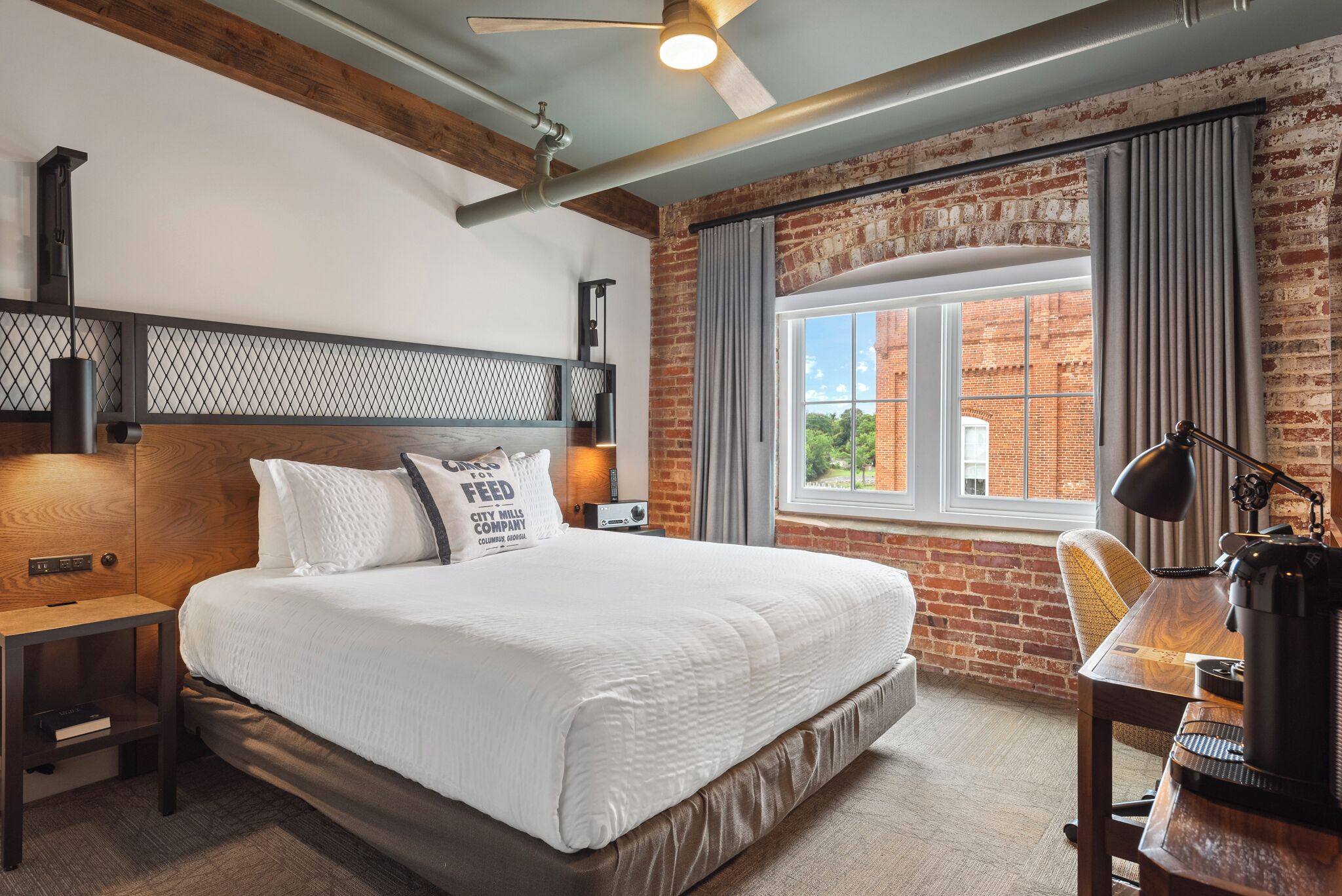 A bedroom with a large bed, a desk, and a window with curtains.