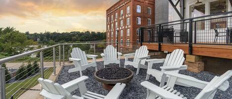 A terrace with Adirondack chairs around a fire pit, overlooking a brick building with "FLEET MEAL" signage.