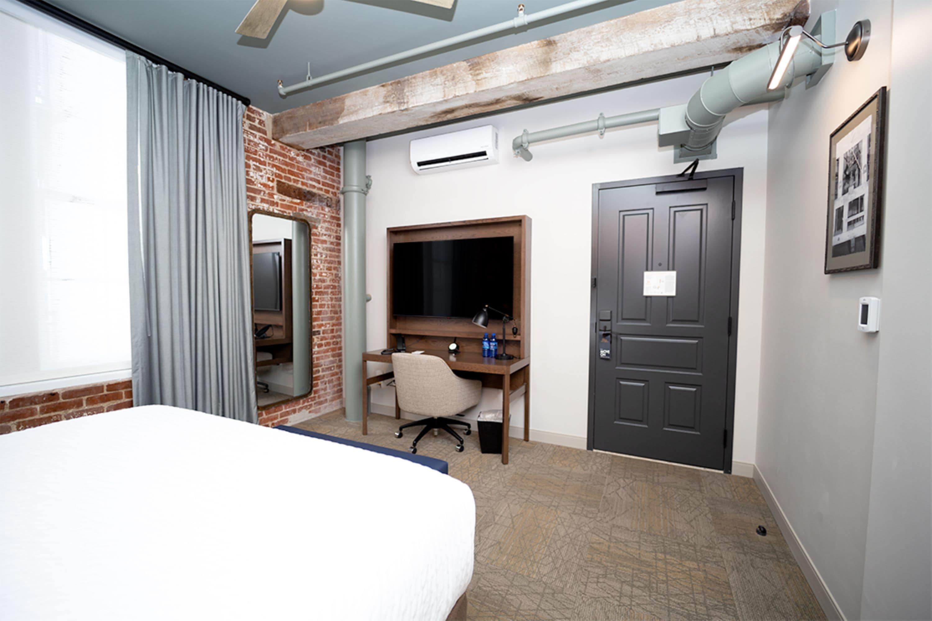 Ein Hotelzimmer mit Bett, Schreibtisch mit Stuhl, Fernseher und einer Tür.