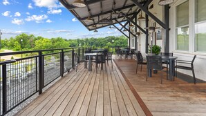 En overdækket terrasse med borde og stole, med udsigt over et grønt landskab.