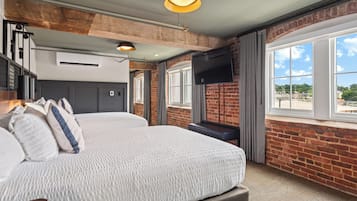 A modern hotel room with a large bed, a flat-screen TV mounted on the wall, and large windows offering a view of the city.