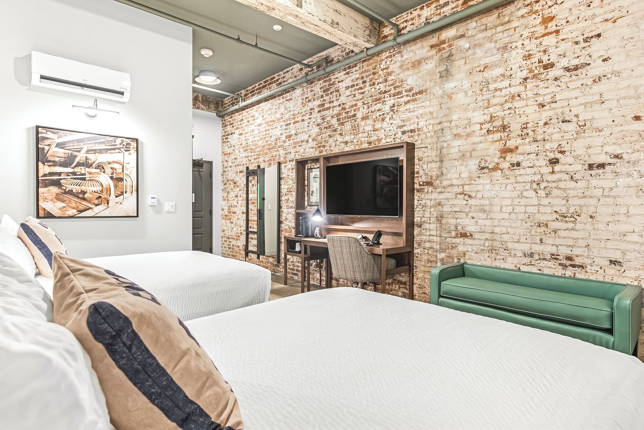 A hotel room with two beds, a desk with a chair, a TV, and a green sofa.