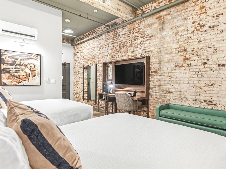 A hotel room with two beds, a desk with a chair, a TV, and a green sofa.