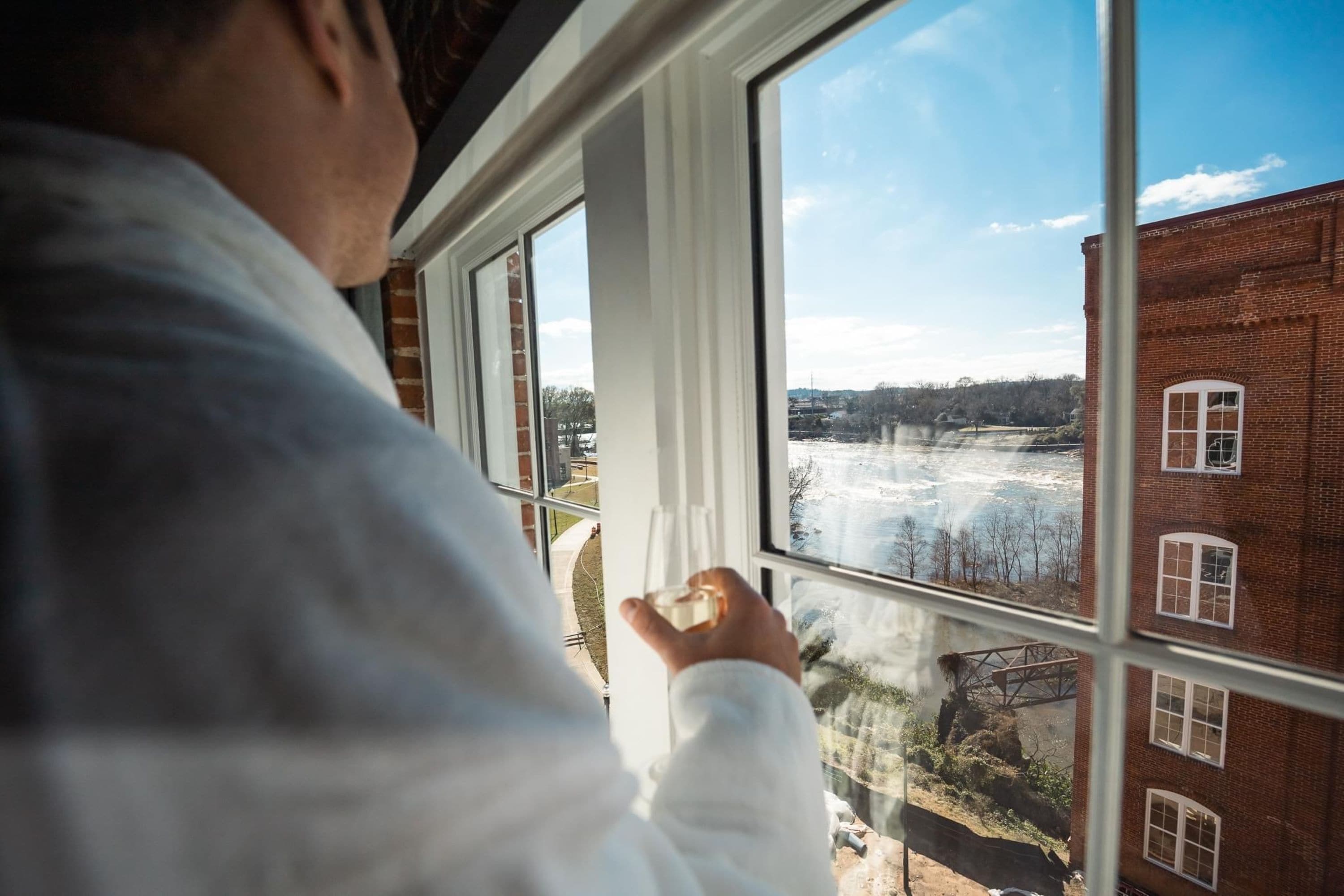 A person looking out of a window at a brick building and a river.