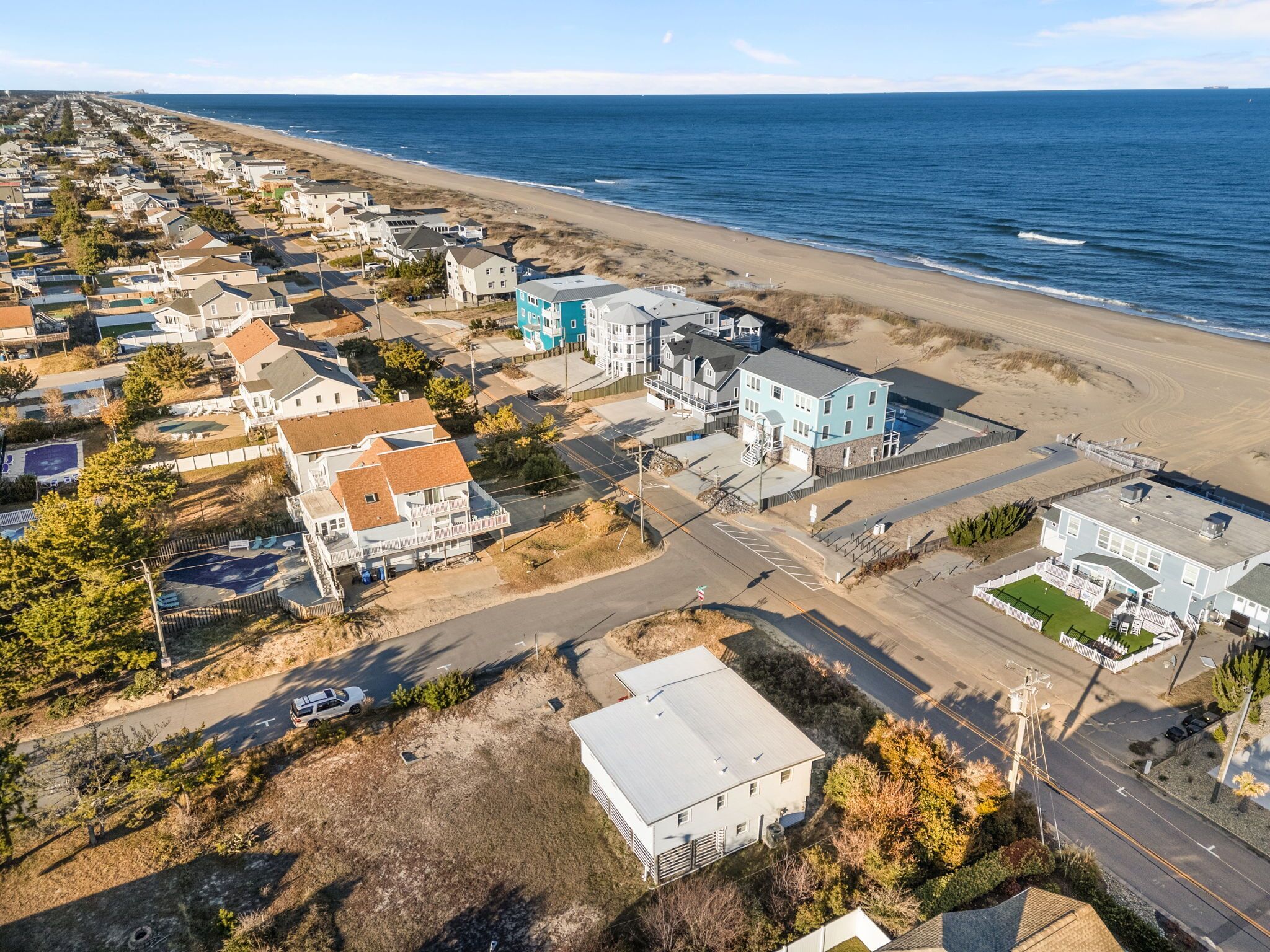 An aerial view of a coastal residential area with houses, a beach, and a road.