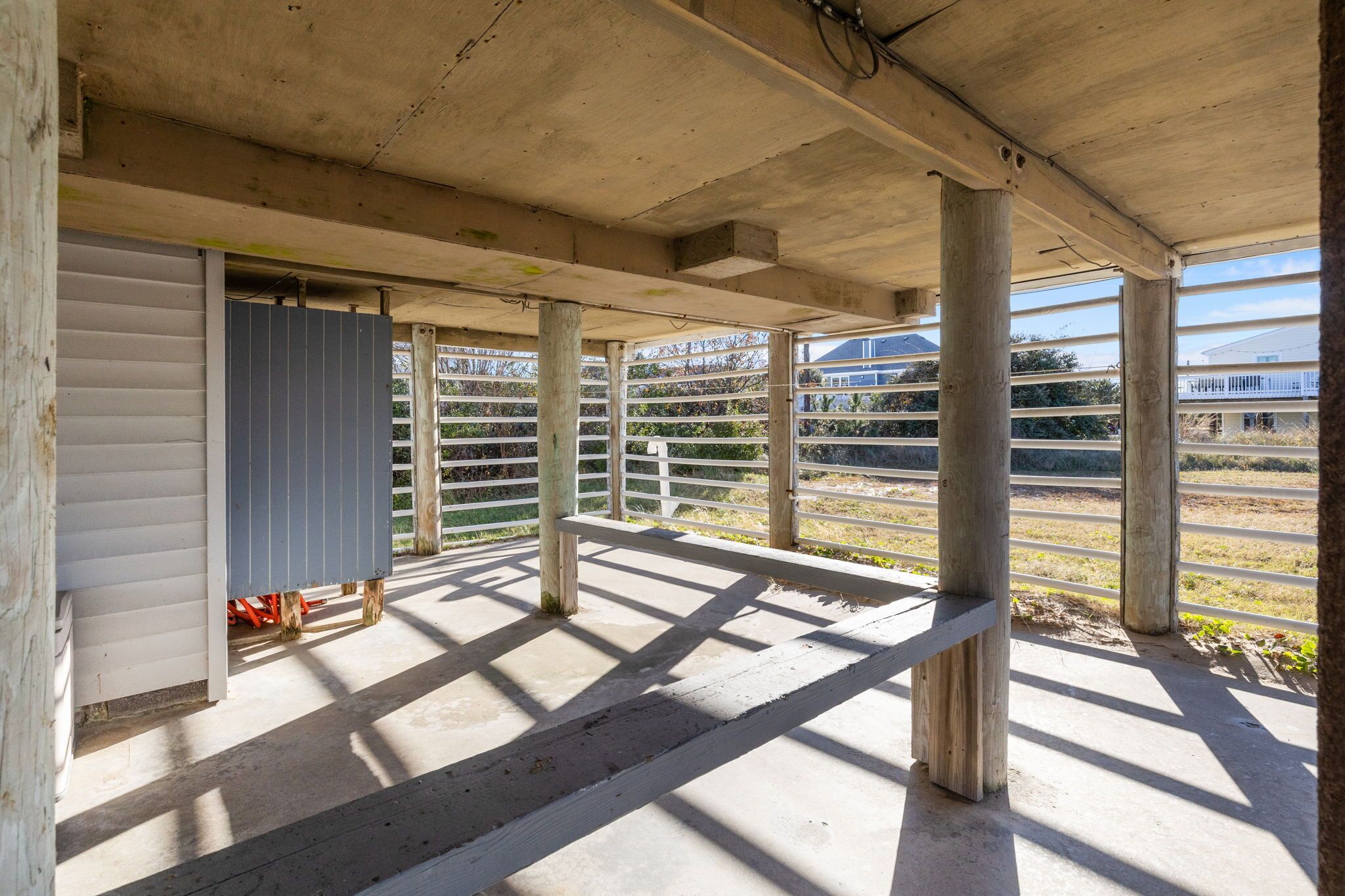 A covered outdoor area with a concrete floor, wooden posts, and a metal fence.