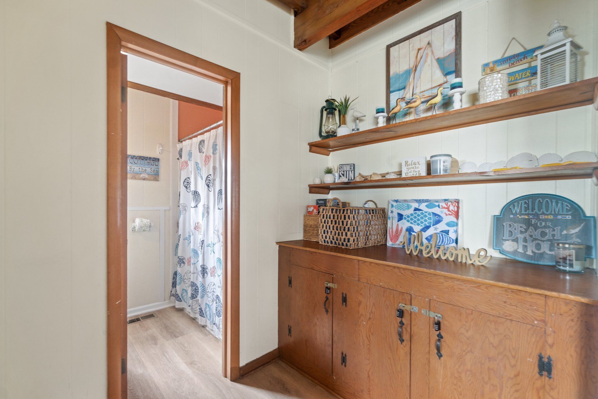 A wooden cabinet with a 'Welcome' sign, shelves with decorative items, and a 'Cottage by the Sea' sign in the background.