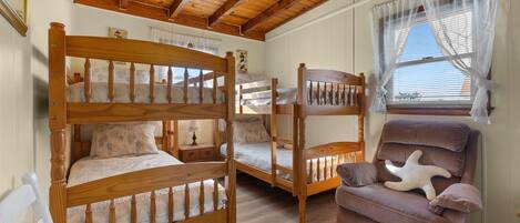 A cozy room with a bunk bed, a cushioned chair, and a window with sheer curtains.