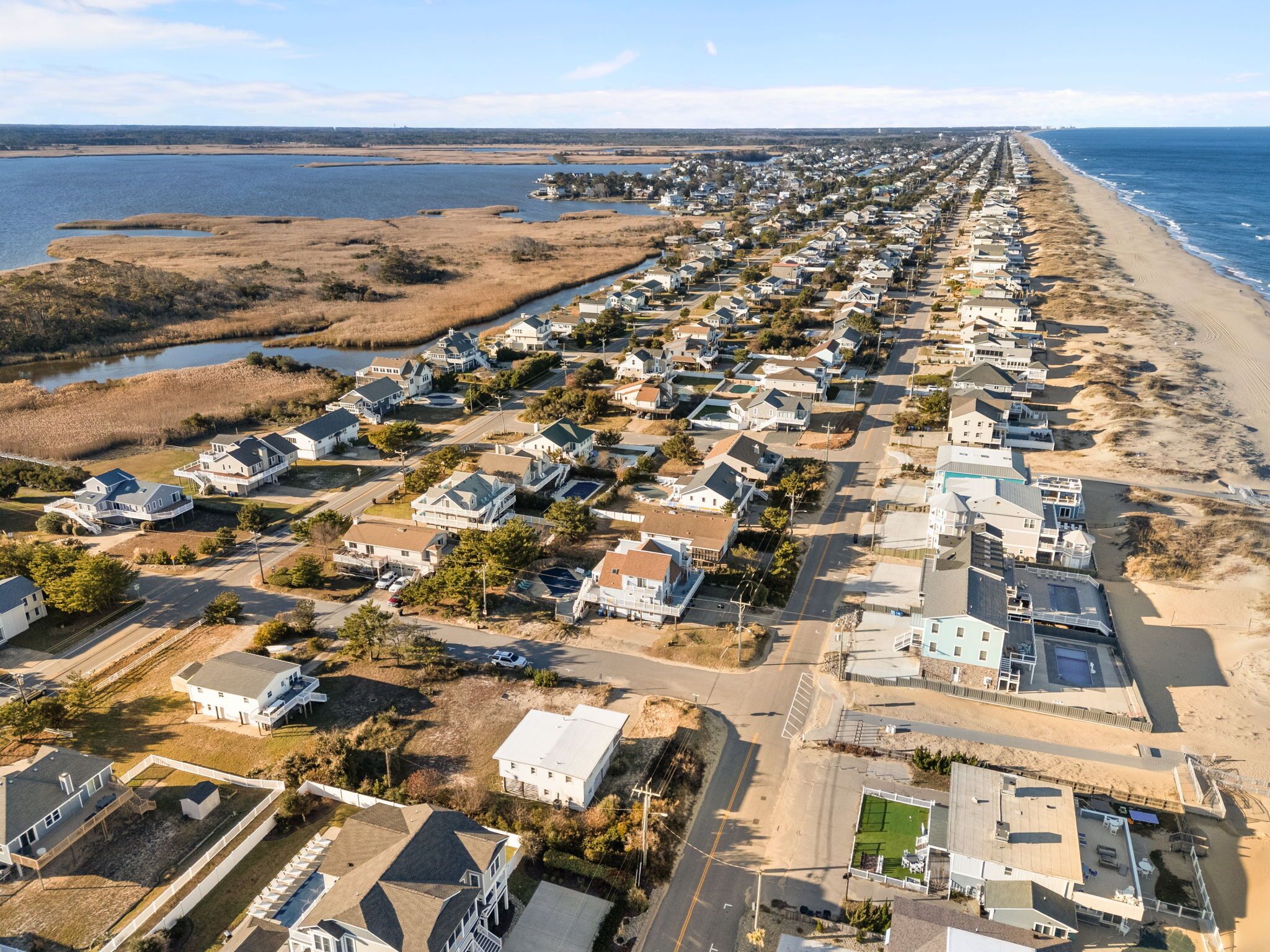A coastal residential area with houses aligned along the beach, featuring a mix of single and multi-story buildings, some with visible balconies and driveways.