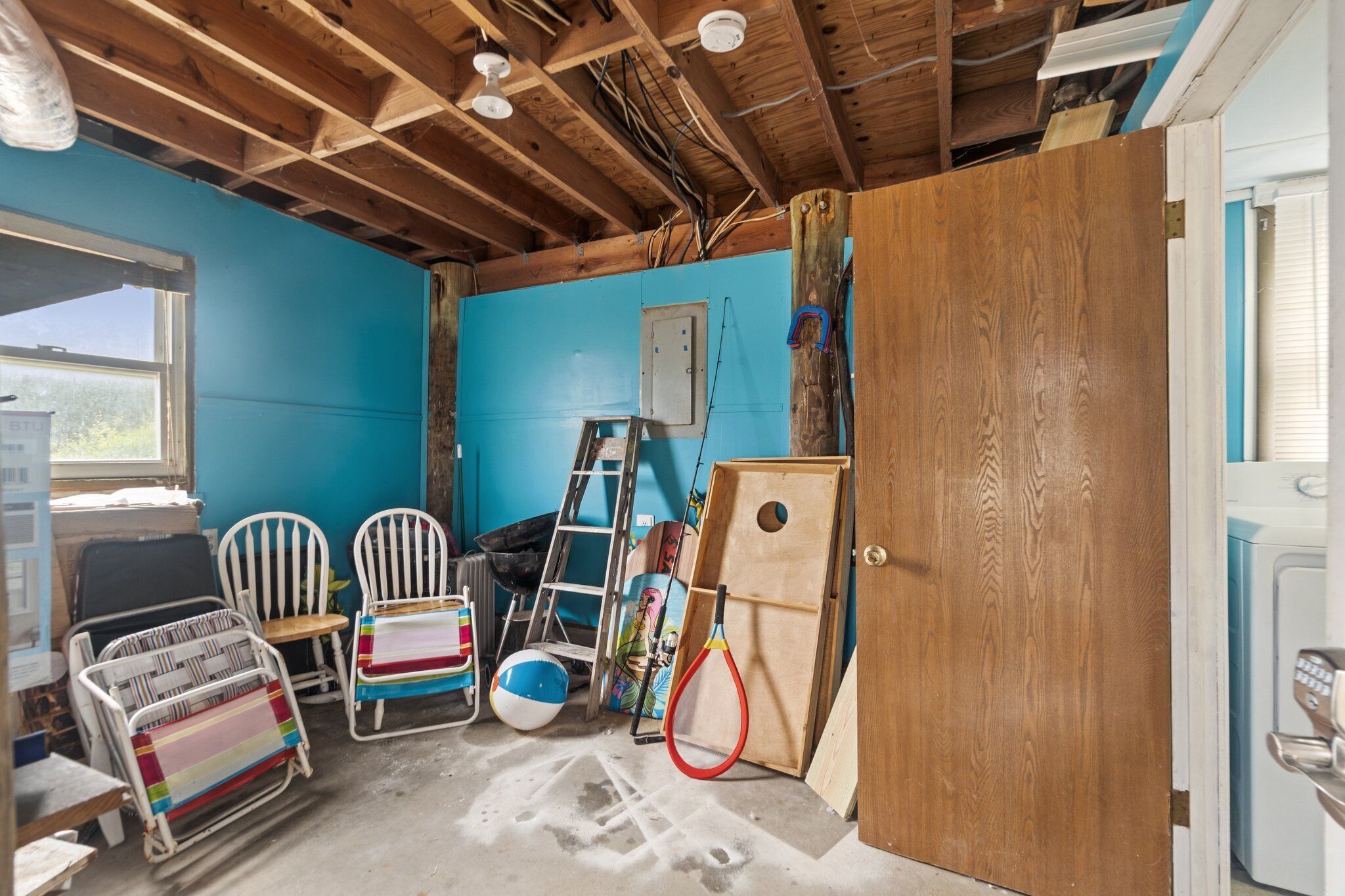 Une pièce avec un mur bleu, des poutres en bois au plafond, une porte et un lave-linge.