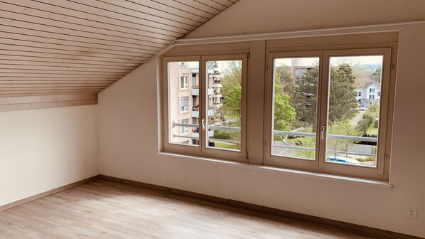 A room with a sloped ceiling, large windows, and a view of a residential area. - Herziges Apartment Mitten im Schoenen Thurgau (Frauenfeld)