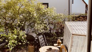 A patio with a table, chairs, a wicker chair, a vase, and a tree with white flowers. - Superior-apartment Near Stuttgart, Garden & Sauna (Kornwestheim)