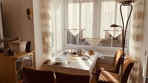 A dining area with a table set for two, a radiator below, and a window with curtains. - Superior-apartment Near Stuttgart, Garden & Sauna (Kornwestheim)