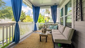A covered porch with a beige sofa, a small table, and blue curtains.
