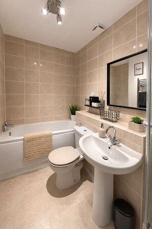 A modern bathroom with a bathtub, toilet, sink, and mirror.
