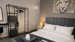 Une chambre à coucher avec un lit, un banc gris, une étagère fixée au mur, un radiateur et un tableau représentant un lion.