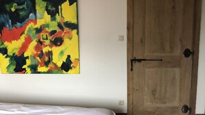 A room with a bed, a wooden door, and a colorful abstract painting on the wall. - 14P 5B Villa de Poothoeve with Sauna and beautiful garden (Bilzen)