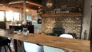 A modern kitchen with a brick fireplace, wooden dining table, and light-colored chairs. - 14P 5B Villa de Poothoeve with Sauna and beautiful garden (Bilzen)