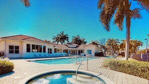 A pool area with a building, palm trees, and a clear sky. - Location, Location, Location (Fort Myers)