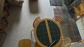 Een gezellige woonkamer met een bank, een houten salontafel en een televisie. Er is een eethoek met een tafel en stoelen. De kamer heeft een groot raam en een open haard.