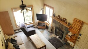 Een woonkamer met een bank, een salontafel, een televisie, een open haard en een trap.