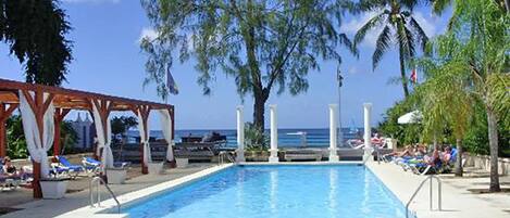 A swimming pool with lounge chairs and umbrellas, surrounded by palm trees and a clear sky.