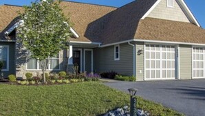 A two-story house with a garage, a well-maintained lawn, and a stone border.