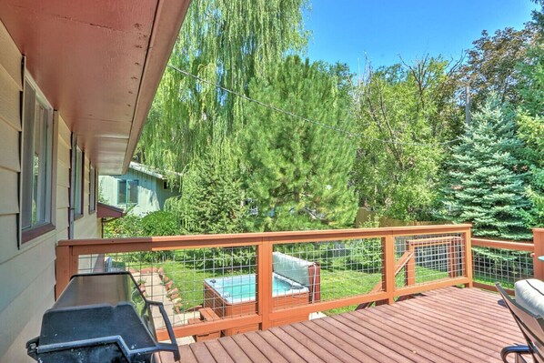 Una terraza de madera con un jacuzzi, una parrilla y vistas a una zona boscosa.