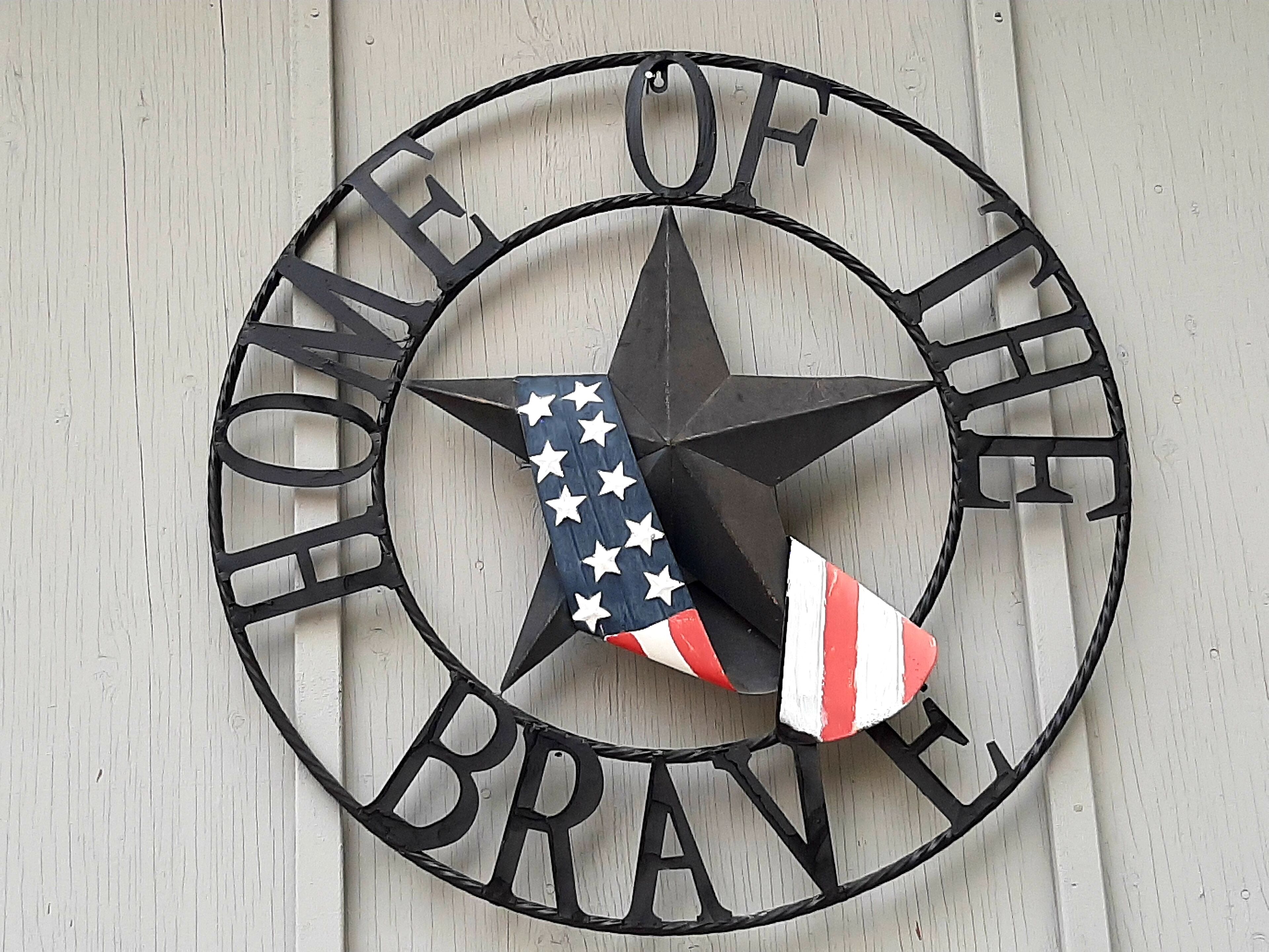 A circular metal sign with a star and American flag design, featuring the text "HOME OF THE BRAVE."