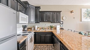 A modern kitchen with dark cabinetry, a white refrigerator, a built-in oven, and a granite countertop.