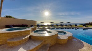 A pool area with tiered hot tubs and lounge chairs, overlooking a body of water.